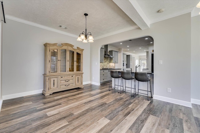 kitchen featuring dark wood-type flooring, a breakfast bar, gray cabinets, decorative backsplash, and wall chimney range hood