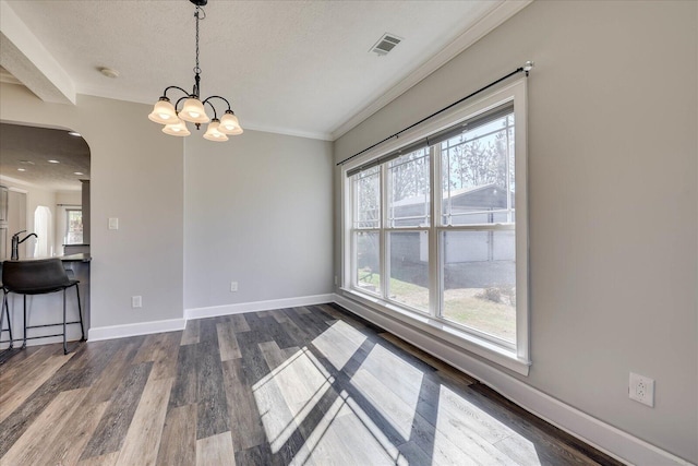 unfurnished dining area with crown molding, dark hardwood / wood-style floors, a chandelier, and a textured ceiling