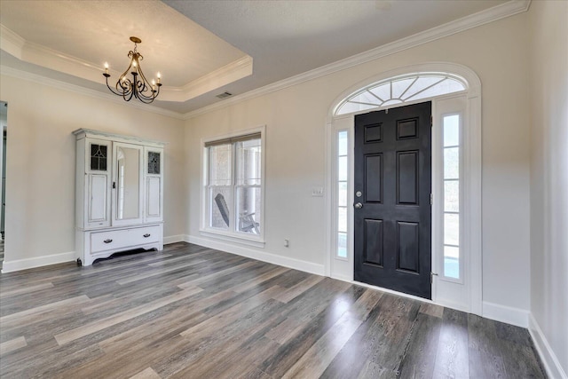 foyer entrance with wood-type flooring, ornamental molding, a raised ceiling, and a chandelier