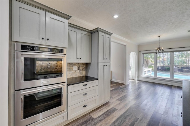 kitchen featuring dark wood-type flooring, gray cabinets, tasteful backsplash, ornamental molding, and stainless steel double oven