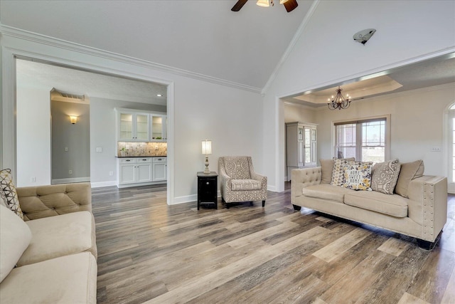 living room featuring hardwood / wood-style flooring, ornamental molding, ceiling fan with notable chandelier, and vaulted ceiling