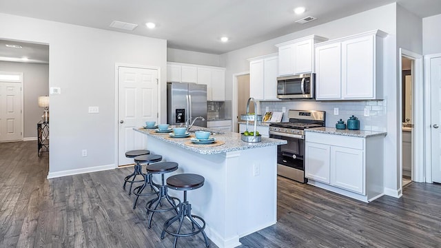 kitchen with dark wood-type flooring, a breakfast bar area, white cabinetry, appliances with stainless steel finishes, and an island with sink