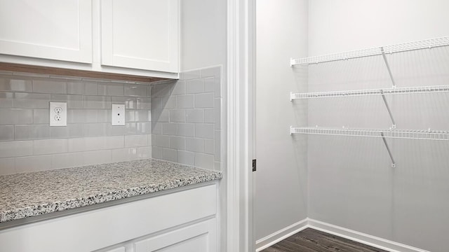 interior space with white cabinetry, dark hardwood / wood-style flooring, light stone countertops, and backsplash