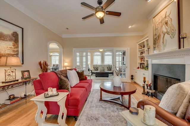 living room with ornamental molding, built in shelves, ceiling fan, and light hardwood / wood-style floors