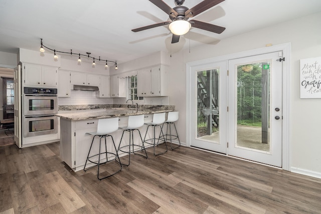 3247 Ramsgate Rd, Augusta, GA 30909 - kitchen featuring under cabinet range hood, white cabinetry, a peninsula, and stainless steel double oven