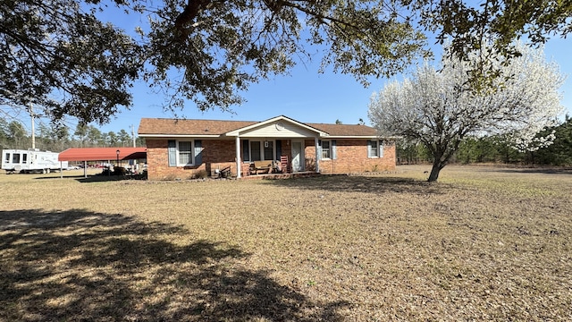 ranch-style house featuring covered porch, brick siding, a carport, and a front yard