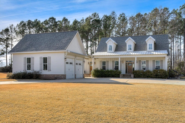 new england style home featuring a porch, a front yard, and a garage