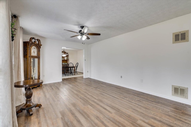 empty room with ceiling fan, visible vents, a textured ceiling, and wood finished floors