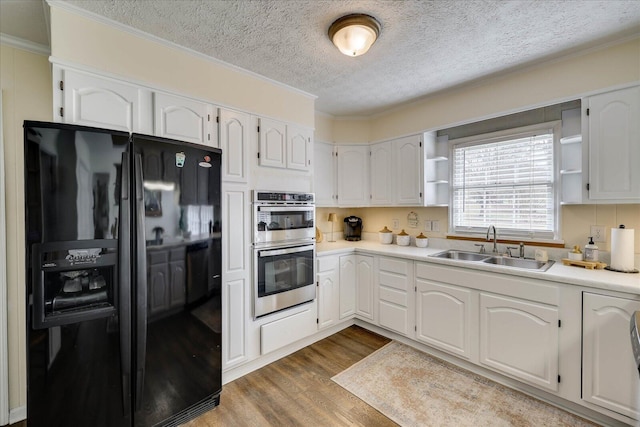 kitchen with double oven, black fridge, wood finished floors, white cabinetry, and a sink