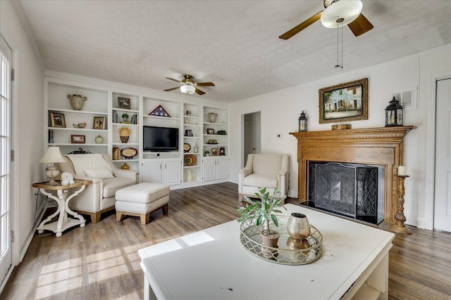 living area featuring a ceiling fan, built in features, a textured ceiling, wood finished floors, and a fireplace