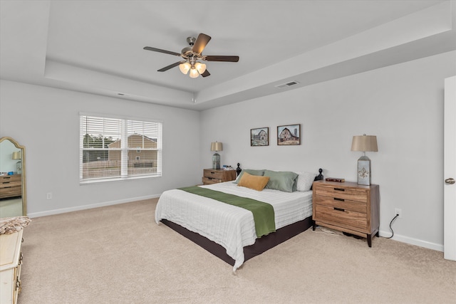 bedroom featuring a tray ceiling, light colored carpet, and ceiling fan