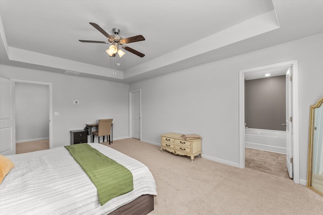 bedroom featuring ensuite bathroom, light colored carpet, ceiling fan, and a tray ceiling