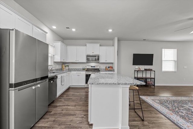 kitchen with a kitchen bar, a center island, appliances with stainless steel finishes, light stone countertops, and white cabinets