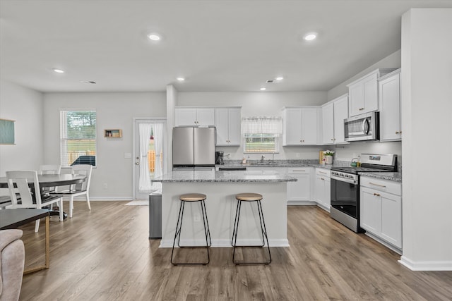 kitchen featuring white cabinetry, appliances with stainless steel finishes, a center island, and light stone counters