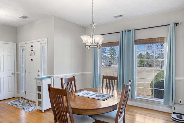 dining room featuring a chandelier, visible vents, light wood-style flooring, and a textured ceiling