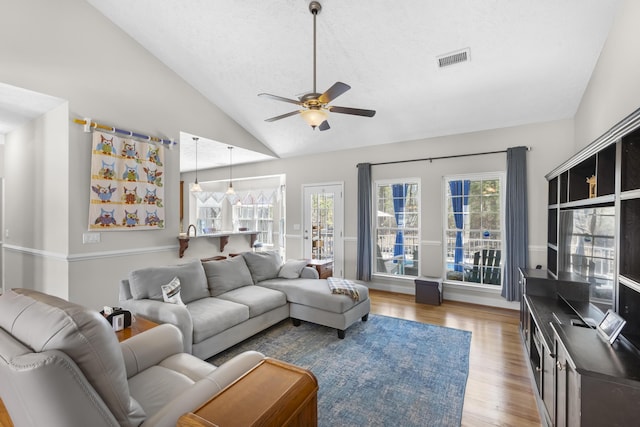 living room featuring visible vents, lofted ceiling, a ceiling fan, and light wood finished floors