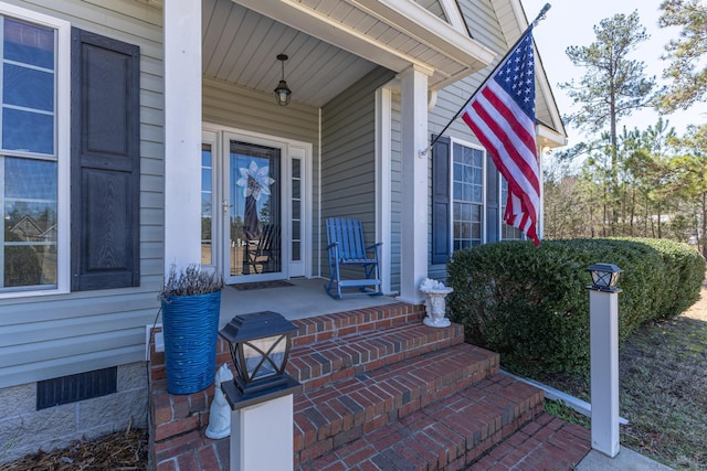 view of exterior entry featuring covered porch and crawl space