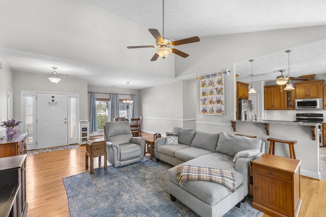 living area featuring lofted ceiling, ceiling fan with notable chandelier, a textured ceiling, light wood finished floors, and baseboards