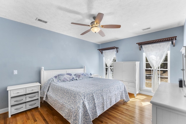 bedroom featuring visible vents, a textured ceiling, a ceiling fan, and wood finished floors