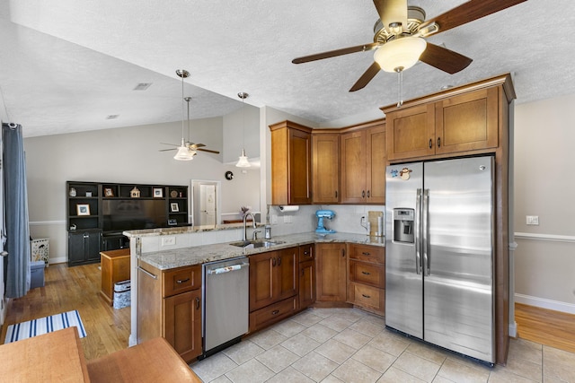 kitchen featuring lofted ceiling, brown cabinets, a peninsula, stainless steel appliances, and a sink