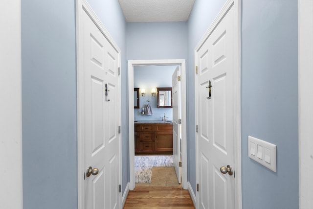 hall with a sink, light wood-style floors, and a textured ceiling