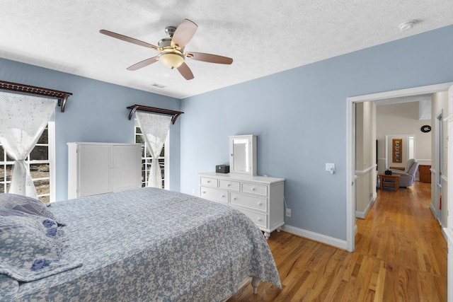 bedroom with visible vents, a textured ceiling, light wood-type flooring, and baseboards