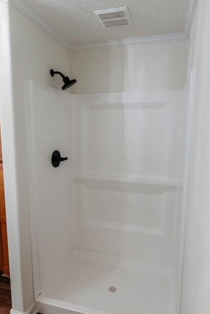 8643 Underwood Rd, Mitchell, GA 30820 - full bathroom featuring crown molding, a textured ceiling, a stall shower, and wood finished floors