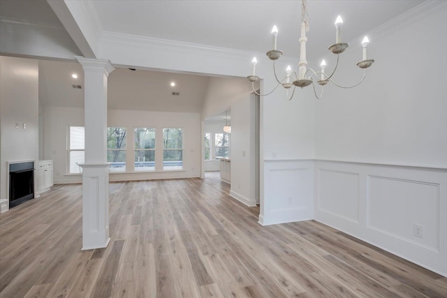 unfurnished dining area featuring lofted ceiling, an inviting chandelier, crown molding, light wood-type flooring, and decorative columns