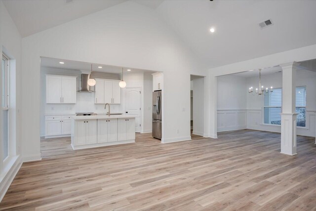 kitchen featuring decorative light fixtures, stainless steel fridge with ice dispenser, wall chimney exhaust hood, a notable chandelier, and white cabinetry