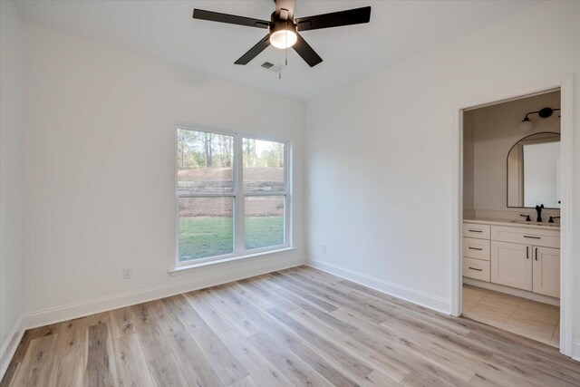 unfurnished bedroom featuring multiple windows, ensuite bathroom, ceiling fan, and light hardwood / wood-style floors