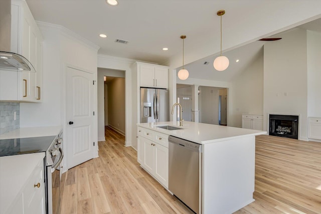 kitchen with sink, wall chimney exhaust hood, stainless steel appliances, an island with sink, and white cabinets