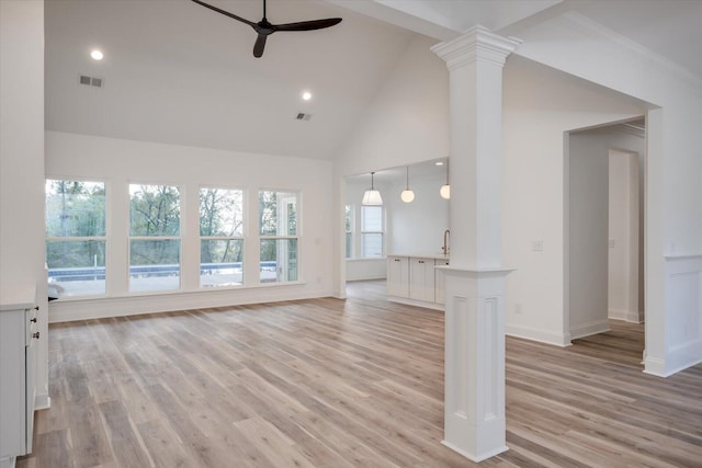 unfurnished living room with ceiling fan, light hardwood / wood-style floors, ornate columns, and high vaulted ceiling