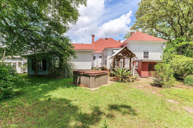 rear view of property featuring a lawn and a hot tub