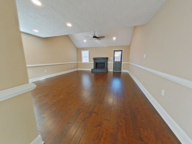 unfurnished living room with vaulted ceiling, a fireplace, ceiling fan, dark wood-type flooring, and a textured ceiling