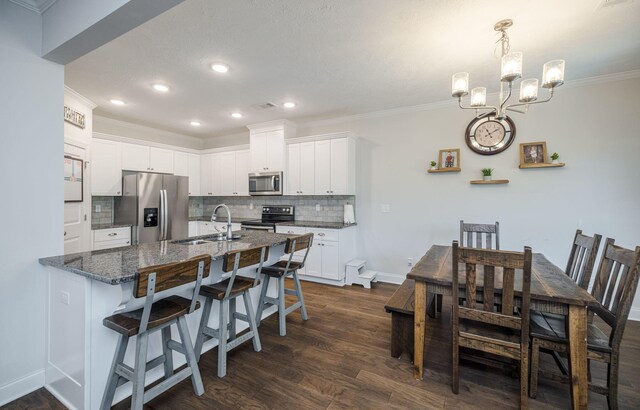 kitchen featuring a breakfast bar, dark stone counters, white cabinets, sink, and stainless steel appliances