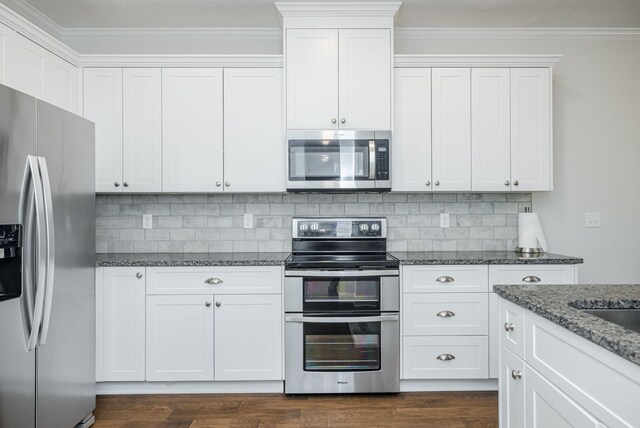 kitchen with white cabinets, backsplash, stainless steel appliances, and dark stone countertops