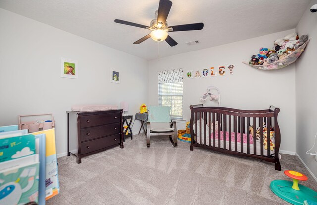 bedroom featuring ceiling fan, a nursery area, and light carpet