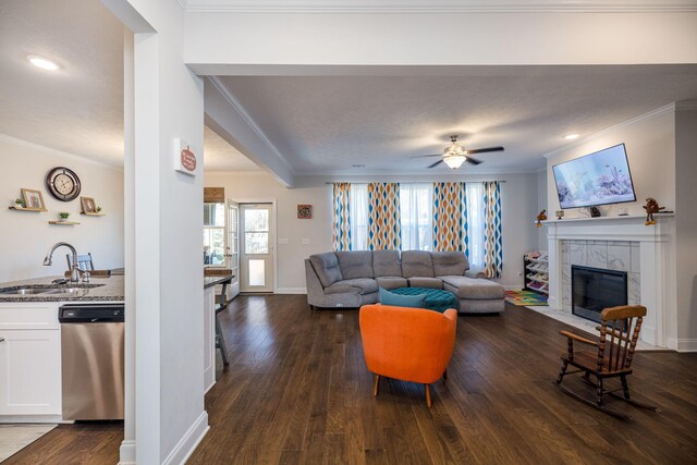 living room featuring ceiling fan, crown molding, sink, and a tiled fireplace