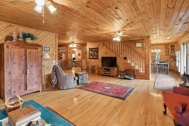 living area with wood walls, ceiling fan with notable chandelier, hardwood / wood-style floors, wood ceiling, and stairway