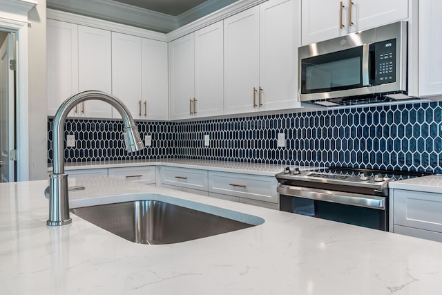 kitchen with backsplash, appliances with stainless steel finishes, white cabinetry, a sink, and light stone countertops