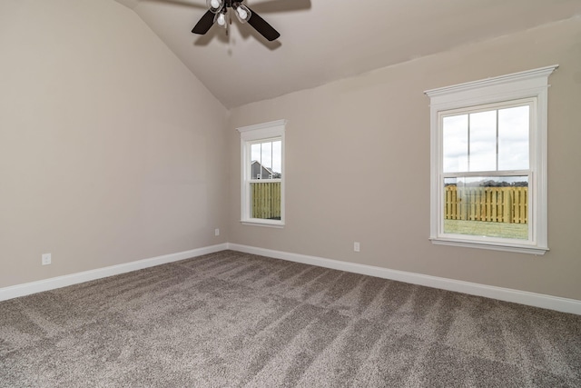 empty room featuring vaulted ceiling, dark carpet, a ceiling fan, and baseboards