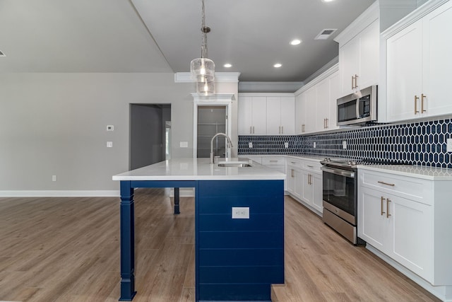 kitchen with stainless steel appliances, a sink, visible vents, decorative backsplash, and an island with sink