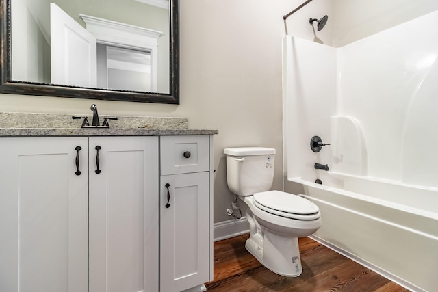 bathroom with baseboards, toilet, wood finished floors, vanity, and shower / washtub combination