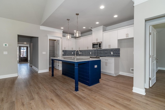 kitchen with tasteful backsplash, an island with sink, stainless steel microwave, a breakfast bar area, and white cabinetry