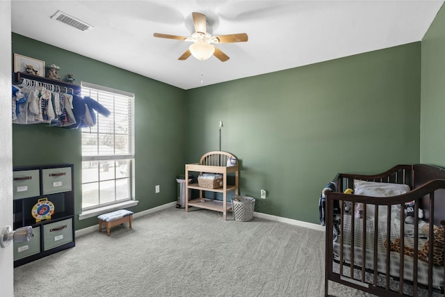 bedroom featuring ceiling fan, carpet flooring, visible vents, baseboards, and a crib