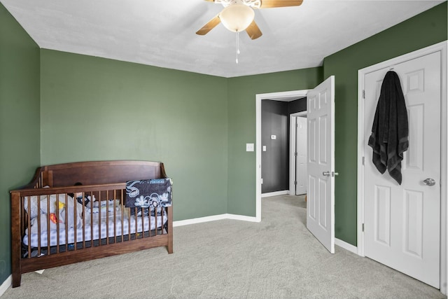 carpeted bedroom featuring a ceiling fan, a nursery area, and baseboards