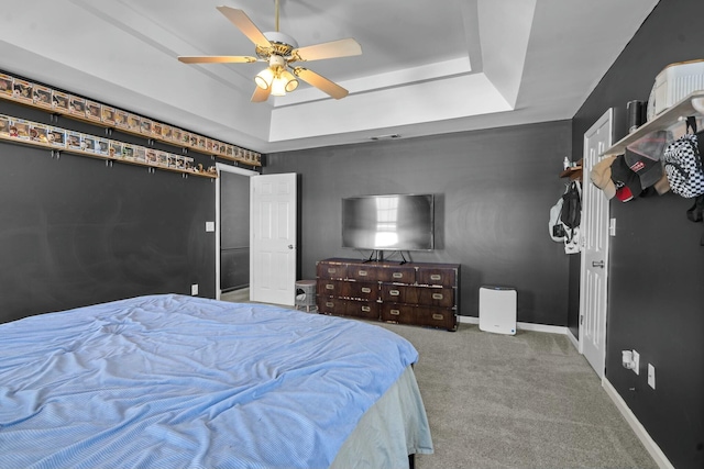 carpeted bedroom with a tray ceiling, a ceiling fan, and baseboards