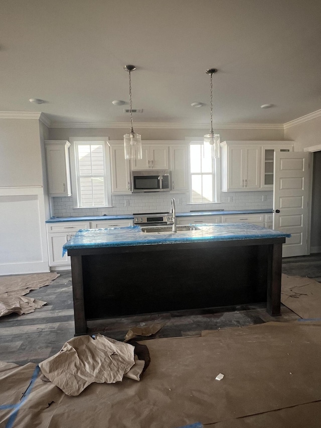 kitchen with a healthy amount of sunlight, a center island with sink, stainless steel microwave, and a sink