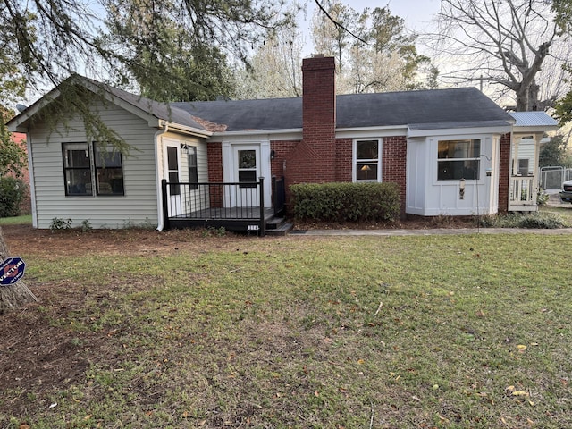 ranch-style house featuring brick siding, a deck, a chimney, and a front yard