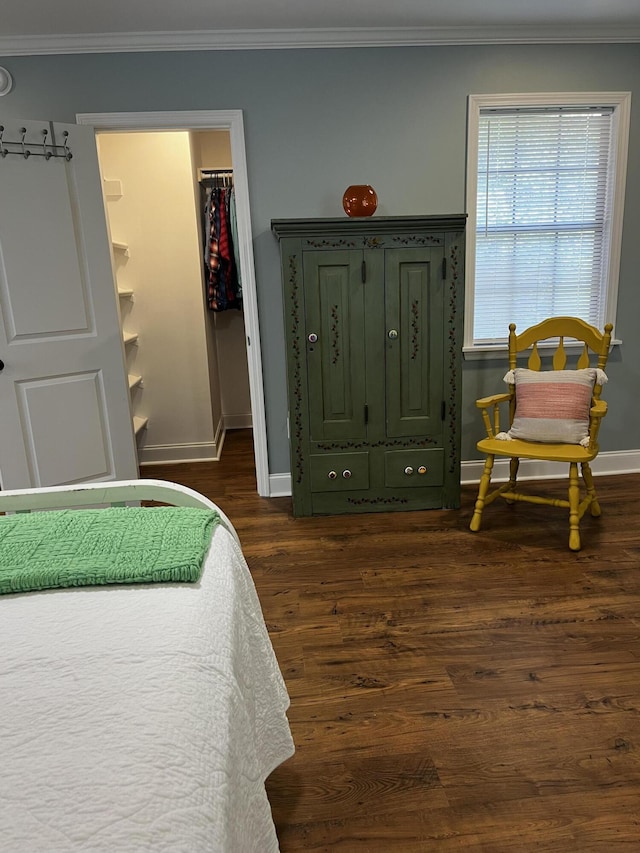 bedroom featuring a walk in closet, ornamental molding, a closet, baseboards, and dark wood-style flooring